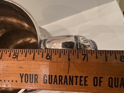 Silver pitcher rim and handle beside a ruler measuring across 5 to 7 inches