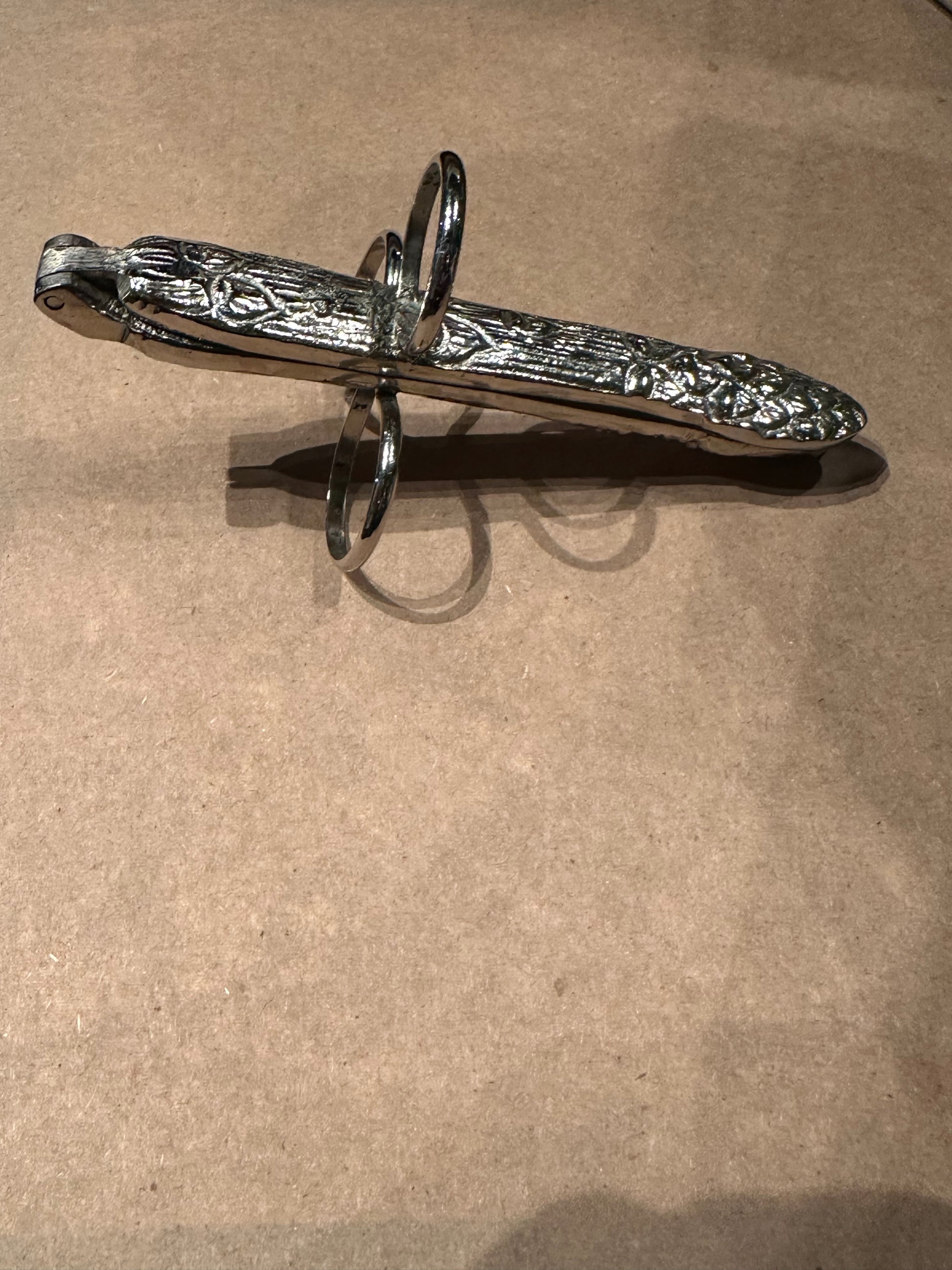 Hinged asparagus utensil at an angle showing embossed handle and finger loops