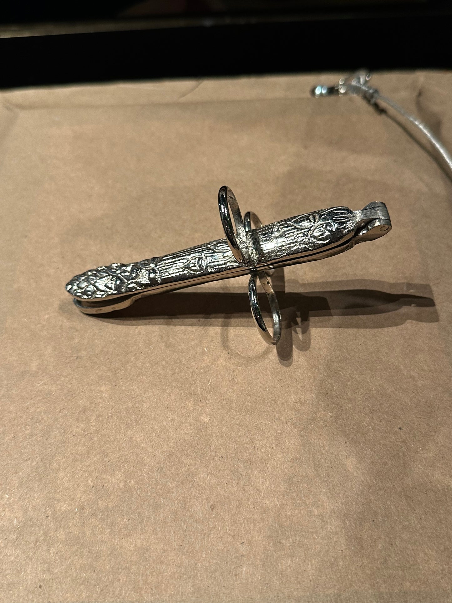 Silver plate asparagus utensil, angled view of foliate handle and three finger loops
