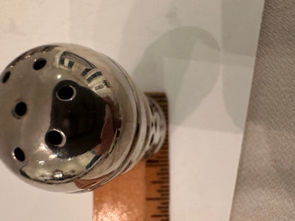 Close-up of a shaker's domed perforated top beside a ruler for scale