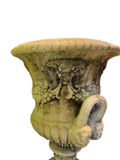 Close-up of a concrete Regency urn's mossy green-patinated body, mask relief and scroll handle