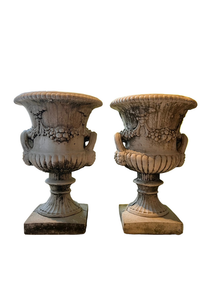 Matched pair of aged concrete Regency urns, front view, classical fruit swags and beaded rims on square plinths