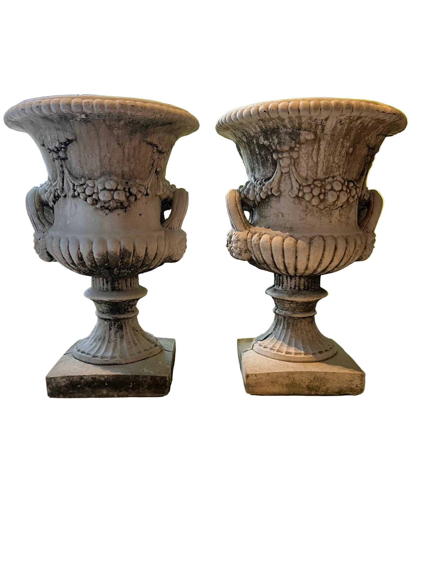 Pair of weathered concrete Regency urns side by side, fluted bodies with fruit-garland relief and scroll handles
