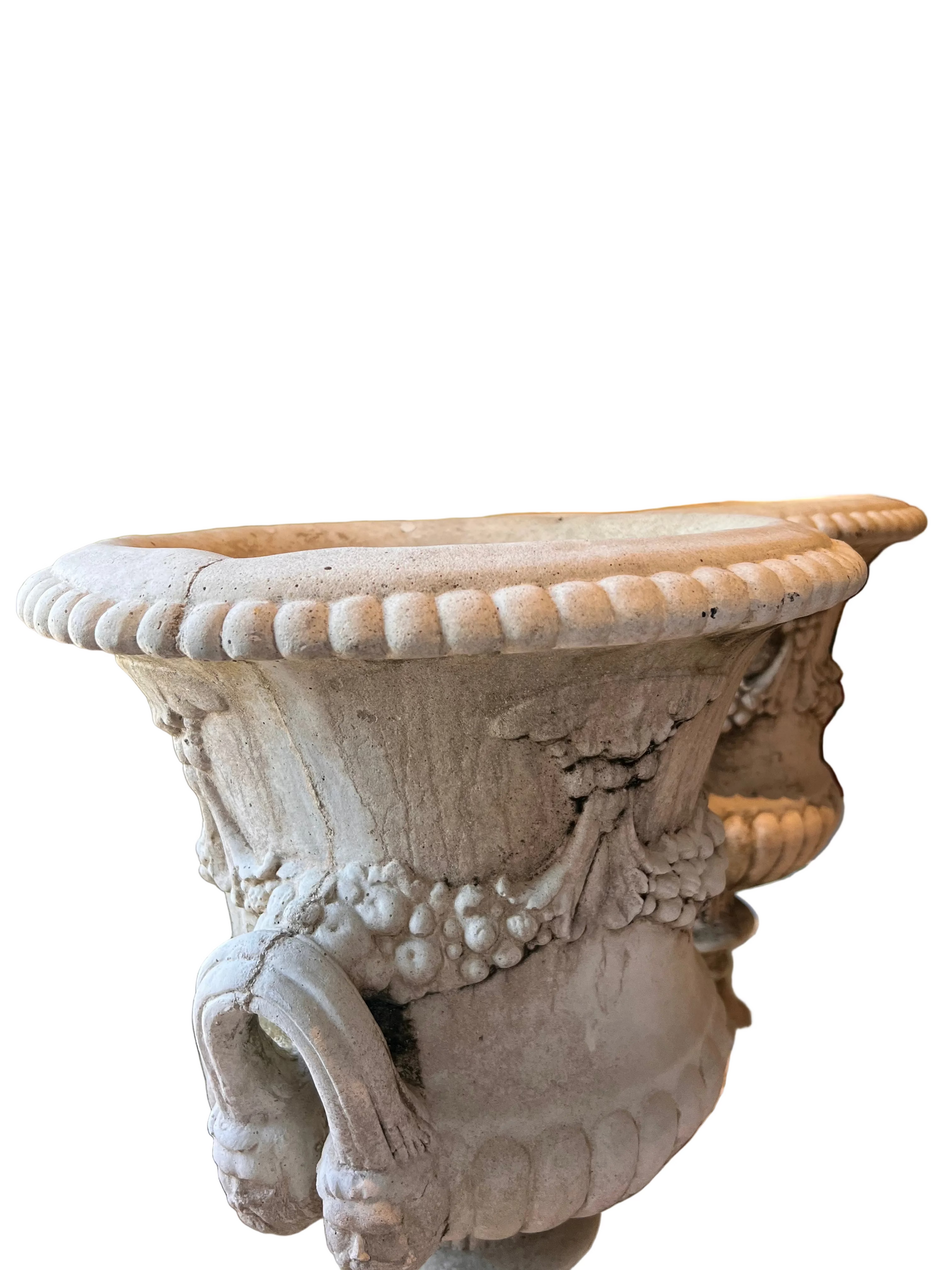 Close-up of one concrete urn's beaded rim and upper bowl with fruit-garland relief and scroll handle