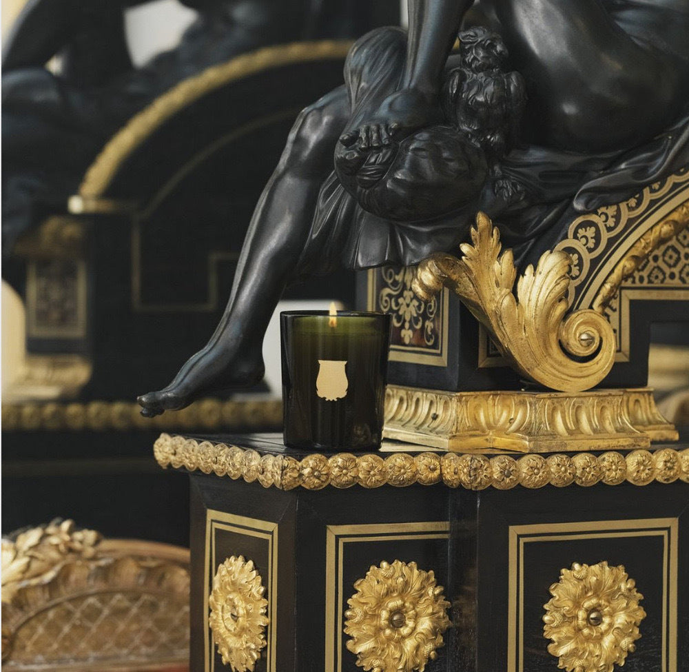Lit Trudon Ernesto candle styled on an ormolu-mounted ebonized cabinet beside a bronze figure.