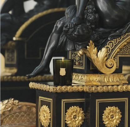 Lit Trudon Ernesto candle styled on an ormolu-mounted ebonized cabinet beside a bronze figure.
