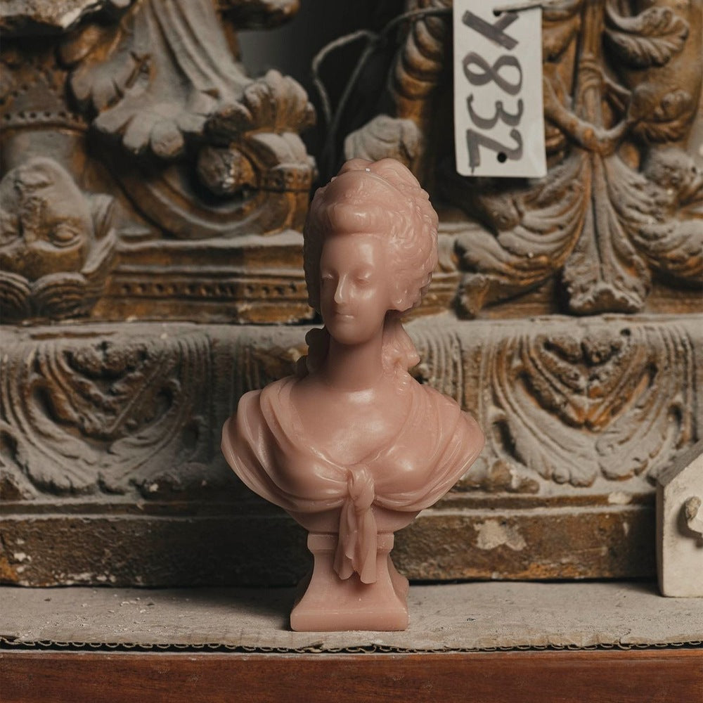 Trudon Marie-Antoinette rose bust candle set before a weathered carved stone ornament