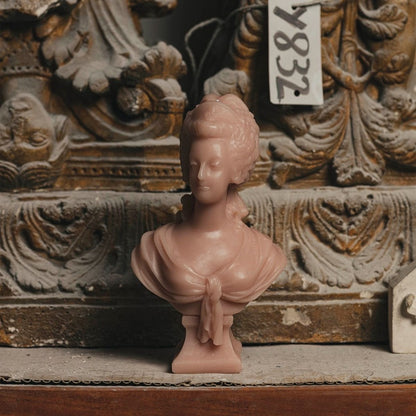 Trudon Marie-Antoinette rose bust candle set before a weathered carved stone ornament