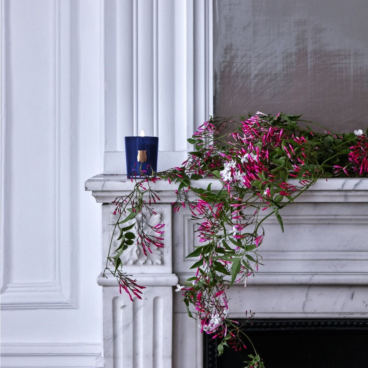 Trudon Madurai petite candle lit on a white marble mantel with cascading pink jasmine