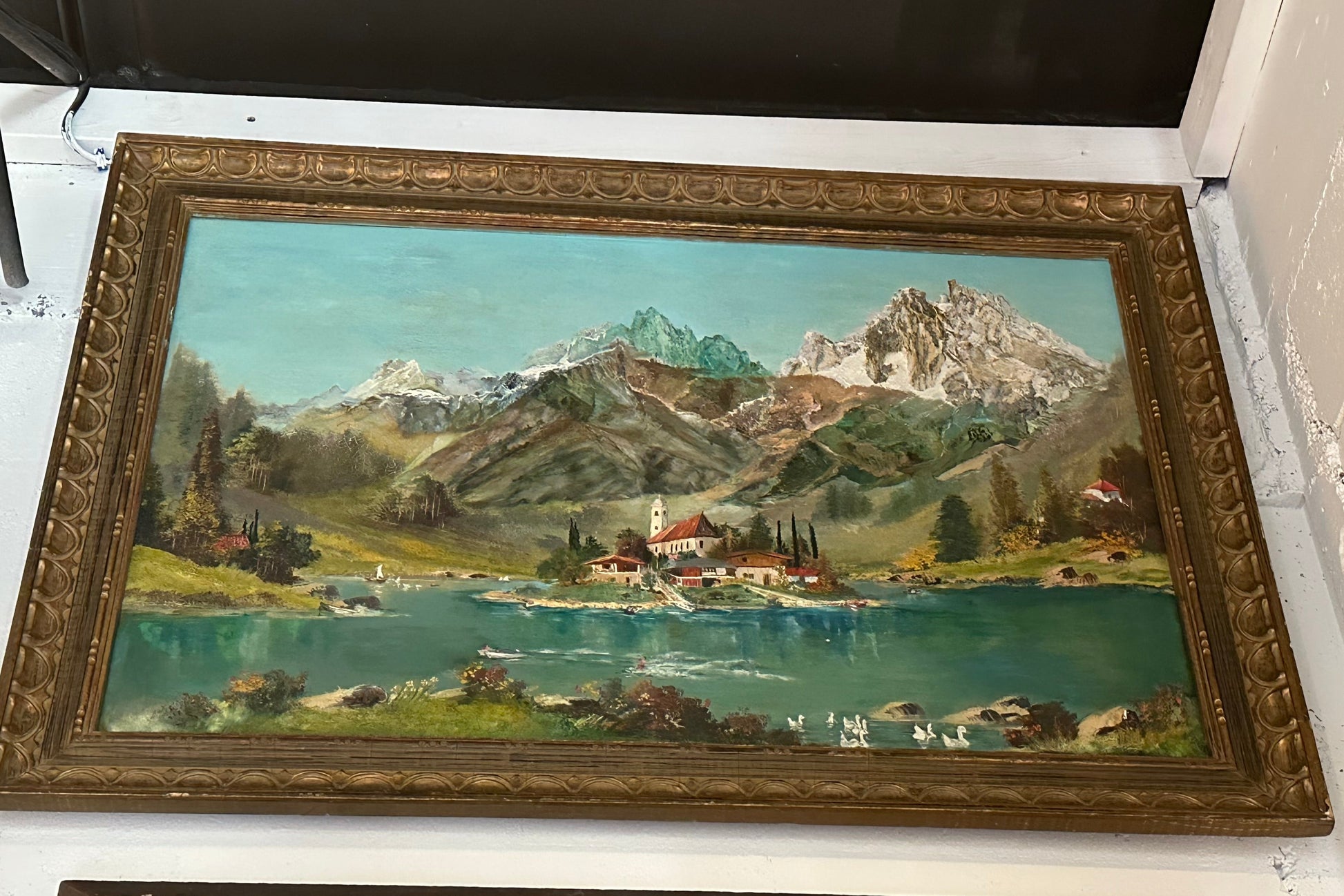 Large-scale framed oil of an alpine lake, island village and snowy peaks, in an ornate carved gilt frame.