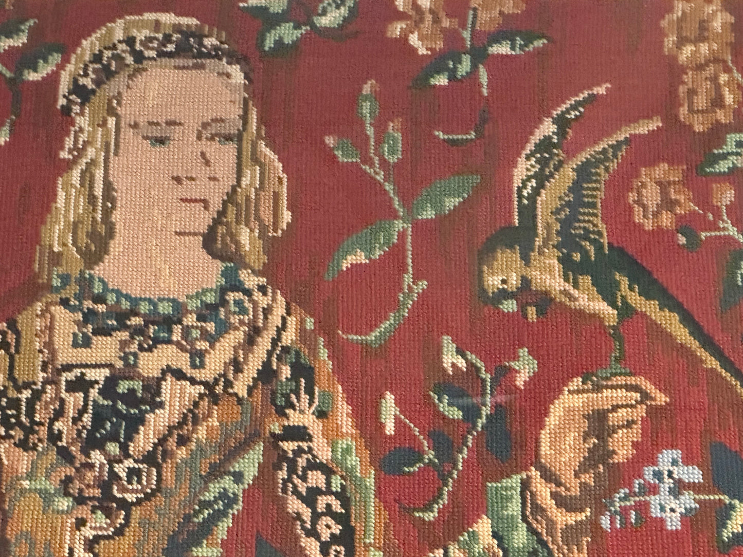 Close-up of the needlepoint medieval lady's face and the perched parrot among foliage