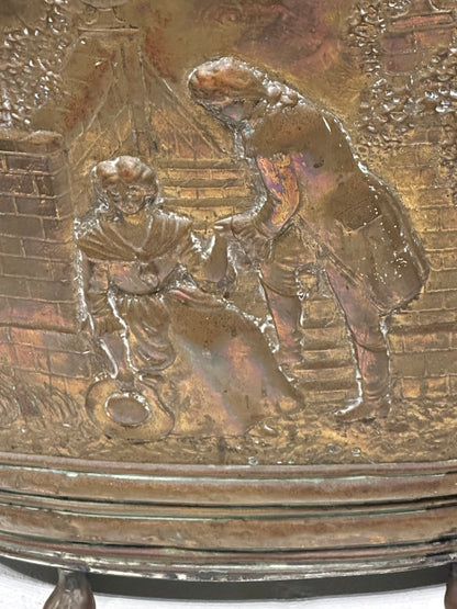 Close-up of brass umbrella stand's repousse scene of two figures by a cottage