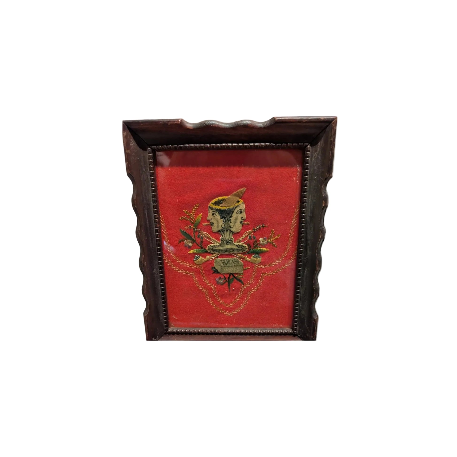 Framed folk art textile with a double-faced figure on red velvet, dark wood frame