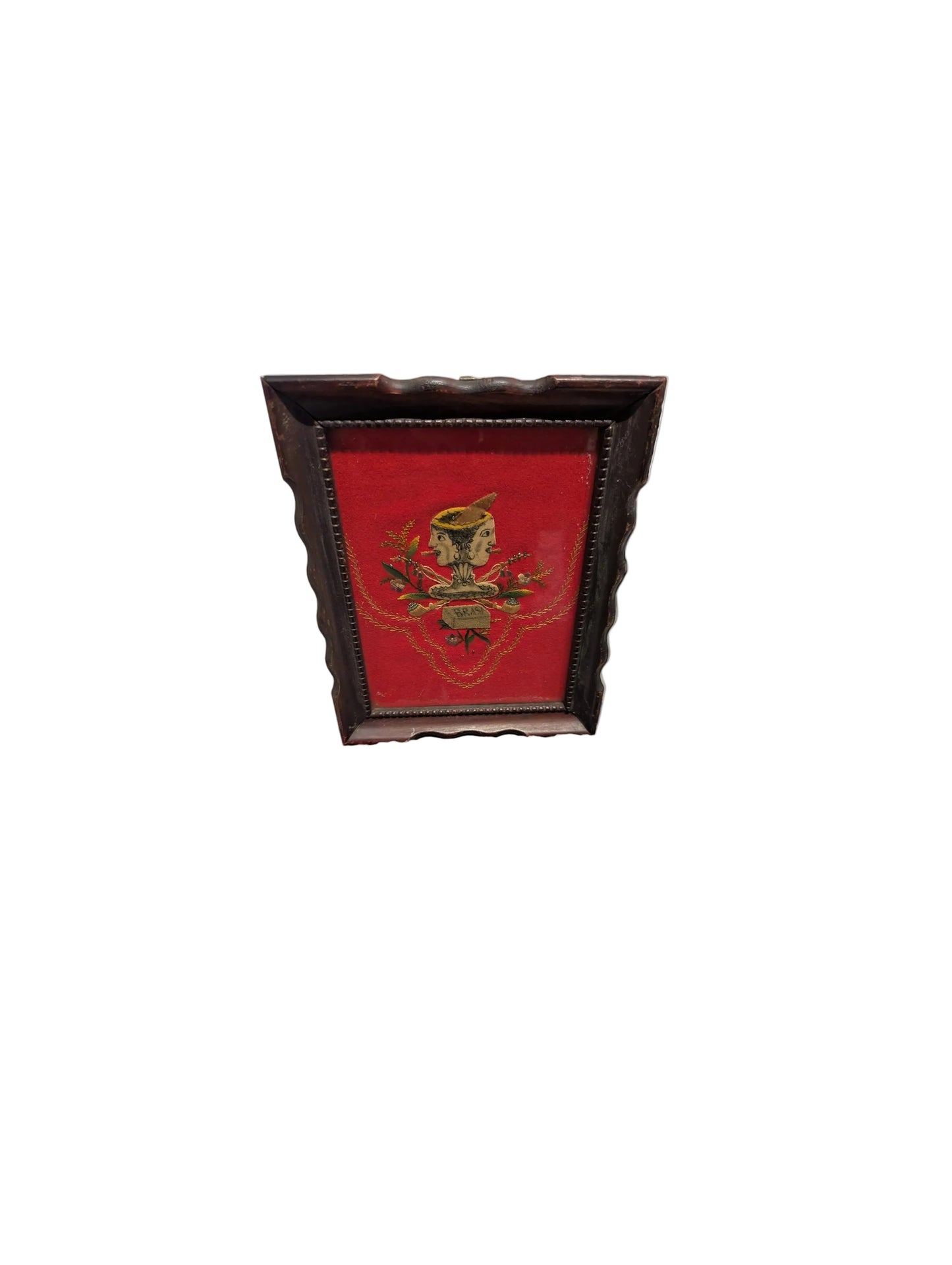 Framed red velvet folk art textile with two-faced head, distant angled view