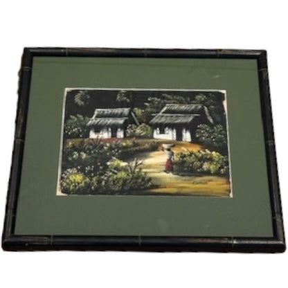 Framed tropical village painting angled left, thatched cottages and a figure, dark bamboo frame