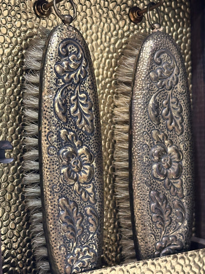 Close-up of two clothes brushes with floral repousse silvered backs against gilt cabinet lining.