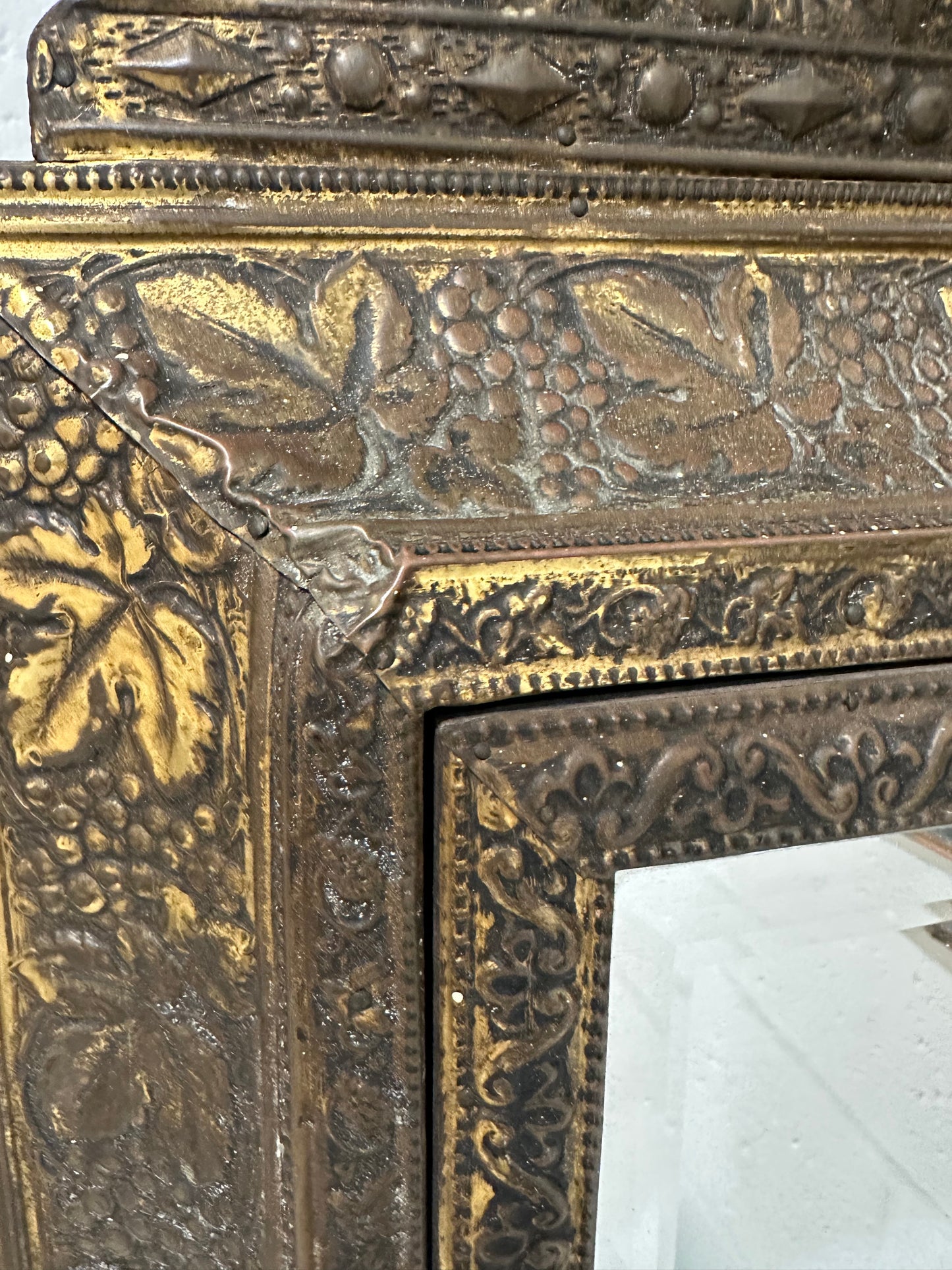 Detail of antique brass cabinet corner with embossed grapevine and beaded borders.