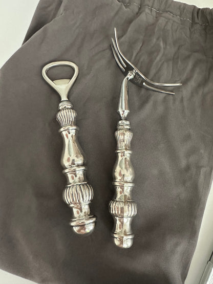 Vintage sterling fluted bar tools, bottle opener and cocktail fork laid on grey cloth.