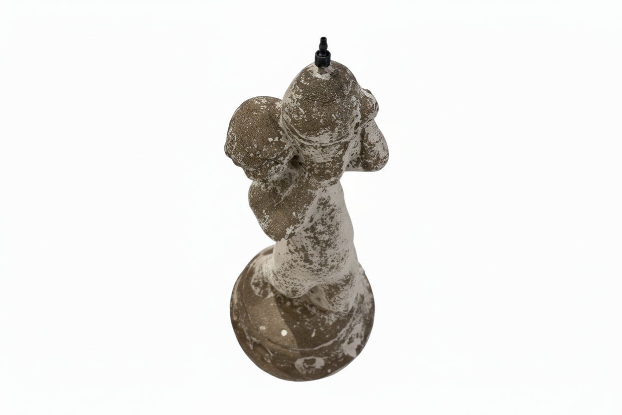 Back view of weathered concrete fountainhead figure with black water spout on head