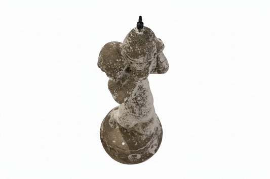 Back view of weathered concrete fountainhead figure with black water spout on head