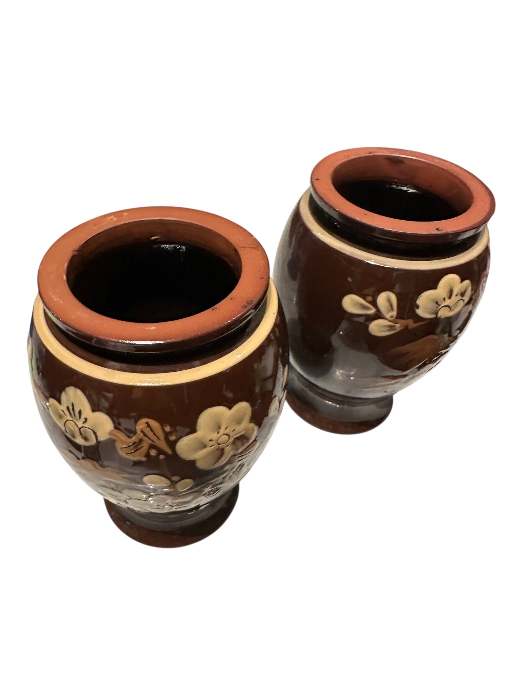 Two brown-glazed floral pottery vases tilted to show terracotta rims and dark glazed interiors