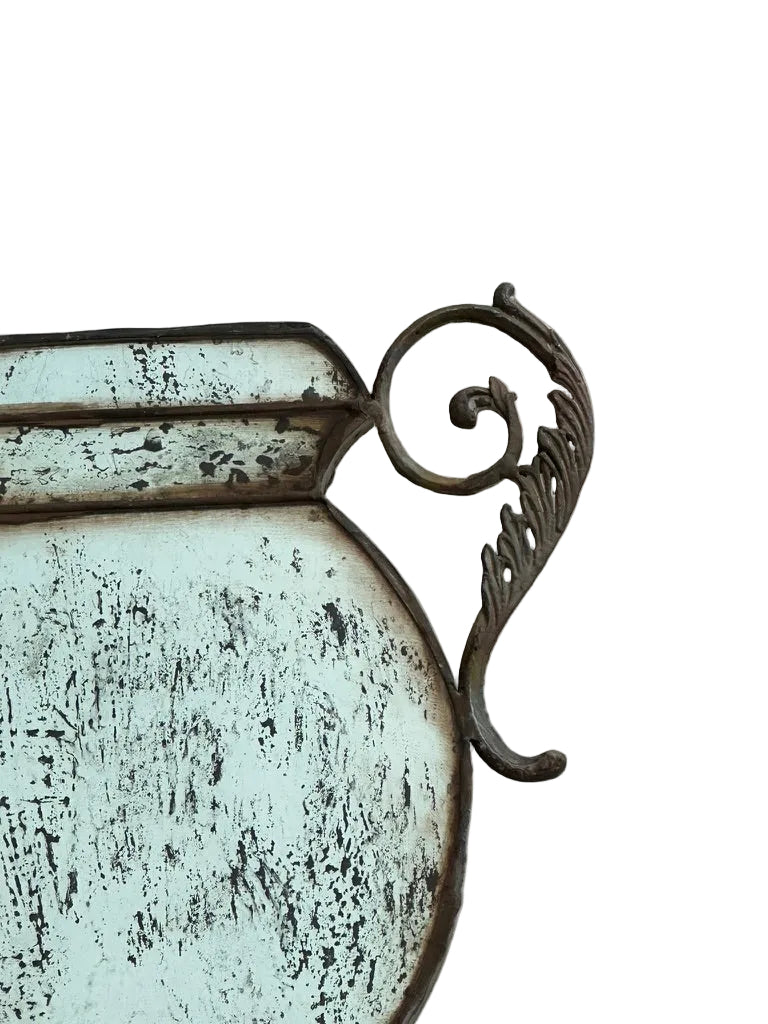 Close-up of the mirrored urn vase's foliate scroll handle and distressed mirror body