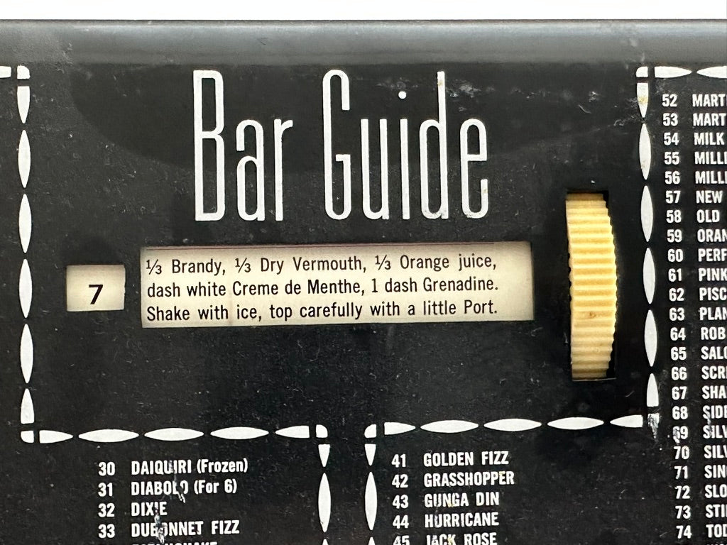 Close-up of MCM Bar Guide face, ivory scroll dial and recipe window listing a brandy cocktail