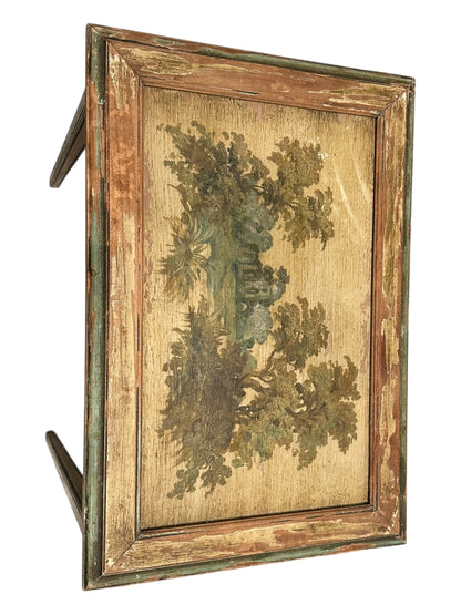 Angled view of one nesting table's painted top showing a foliage landscape and distressed frame.