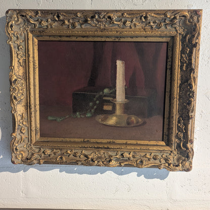 Gilt-framed still life with candlestick and box, angled view hung on a white wall