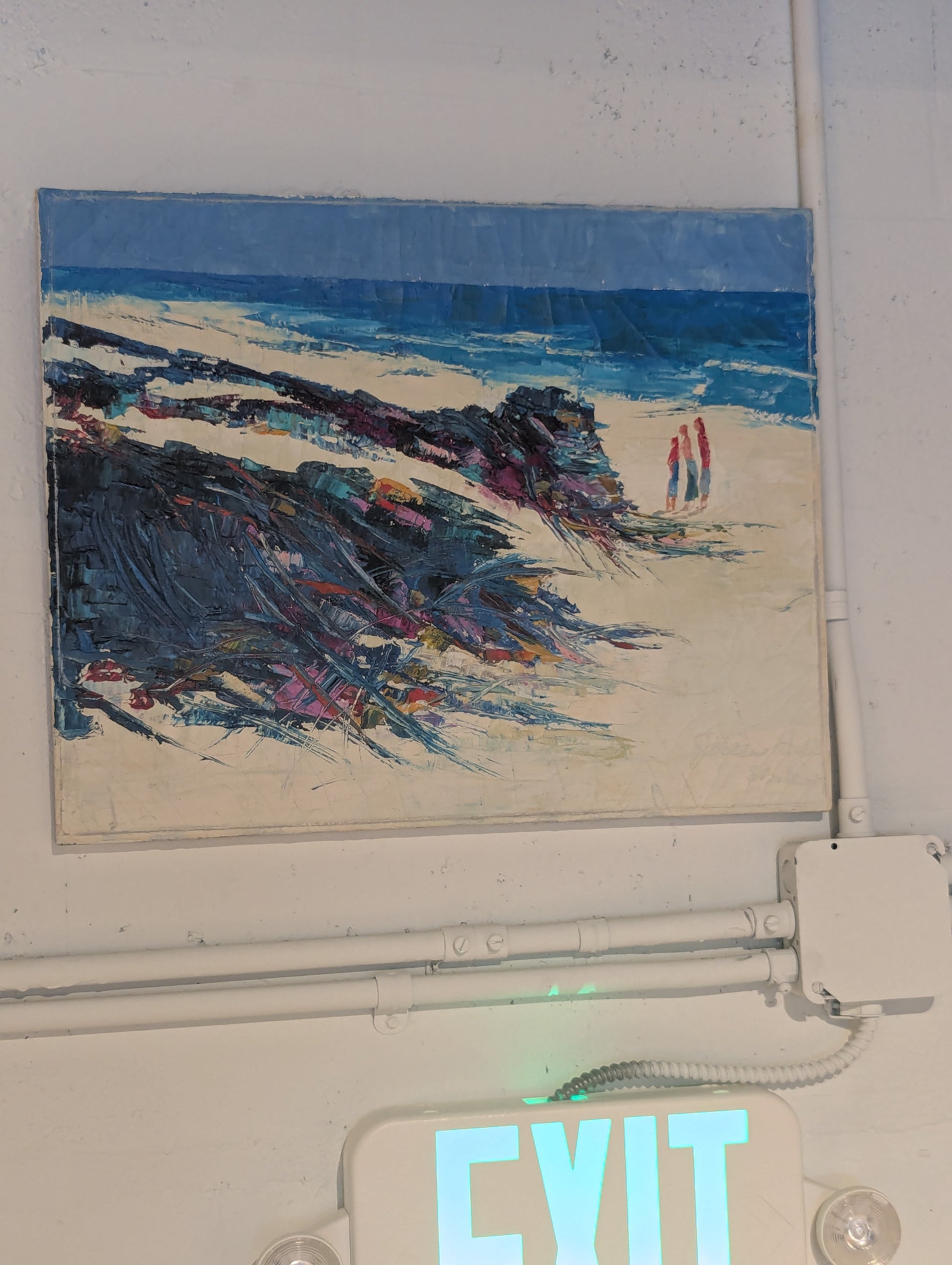 The coastal beach oil painting shown hanging on a wall above an illuminated EXIT sign