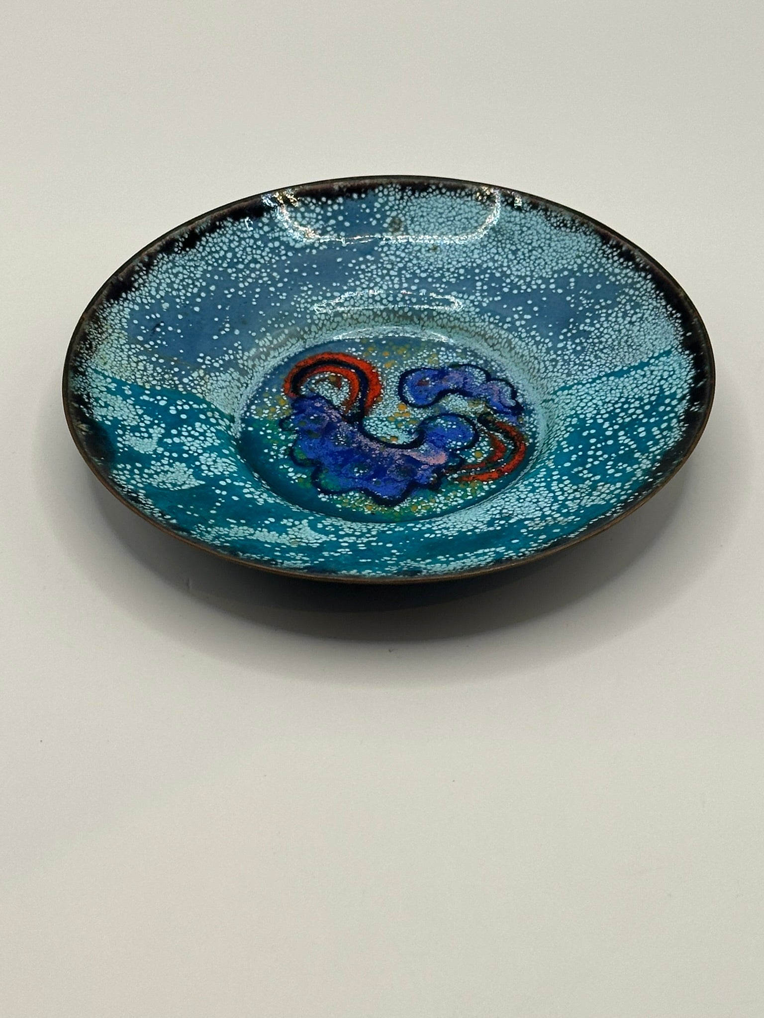 Doris Hall turquoise enamel dish, angled three-quarter view showing dark rim and blue-red center