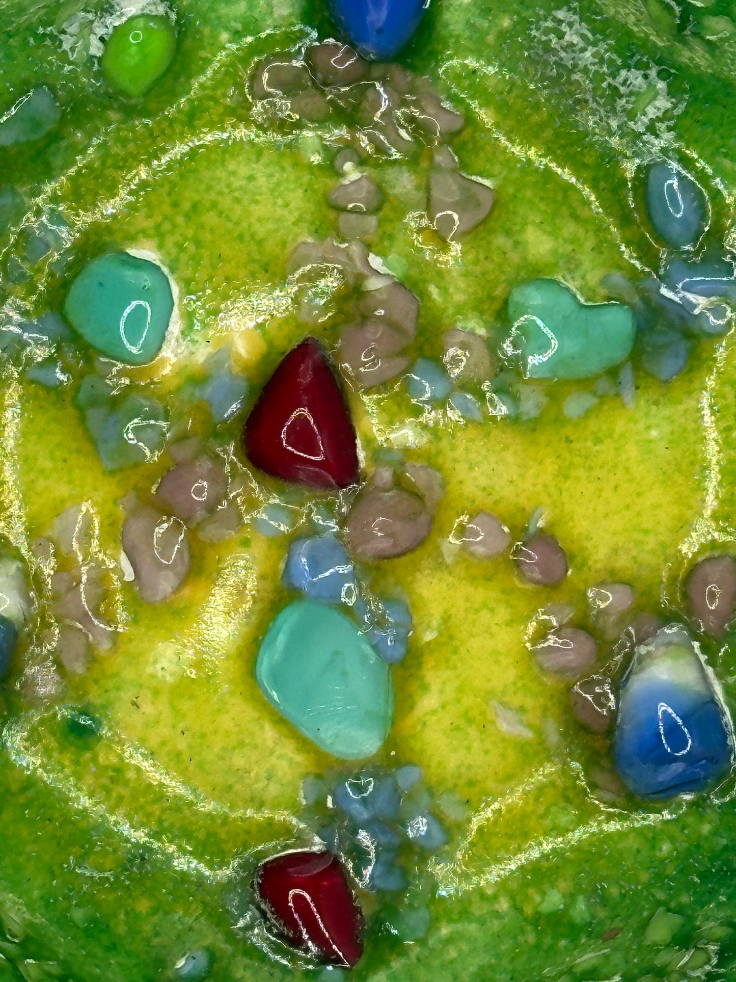 Close-up of fused blue, red and turquoise glass stones set in green and yellow enamel