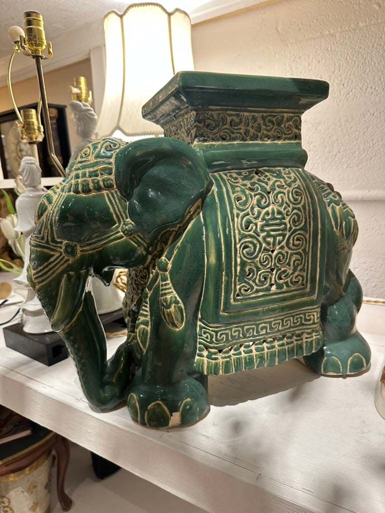Green ceramic elephant garden stool on a shelf, showing embossed blanket and curled trunk