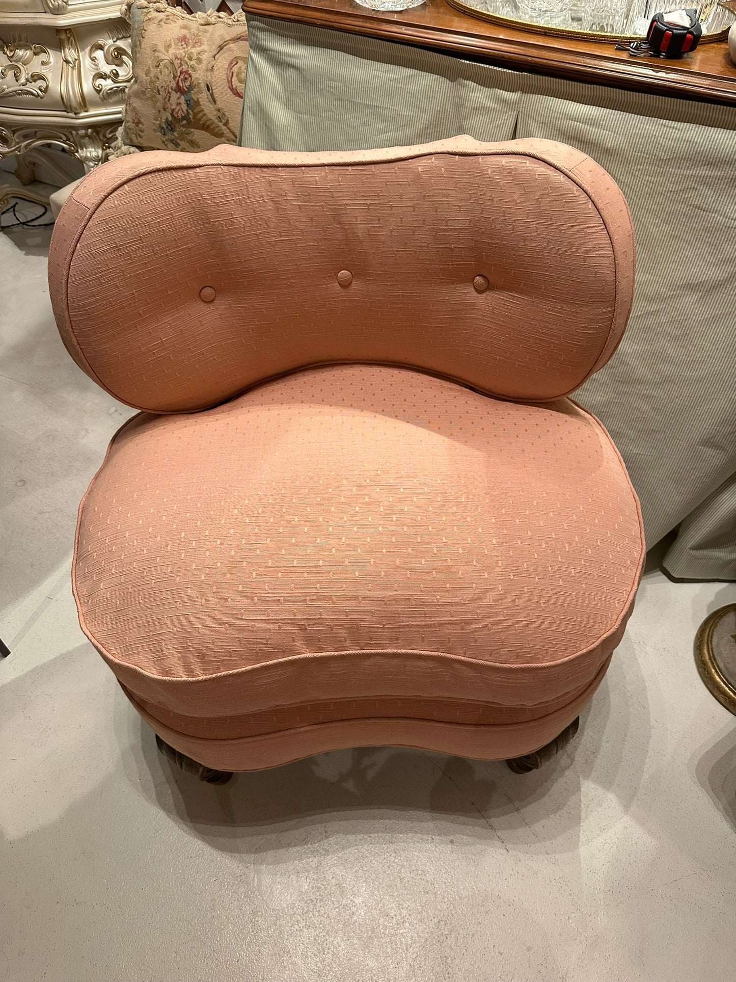 Antique pink coral boudoir chair, front view in showroom showing tufted back and curved seat