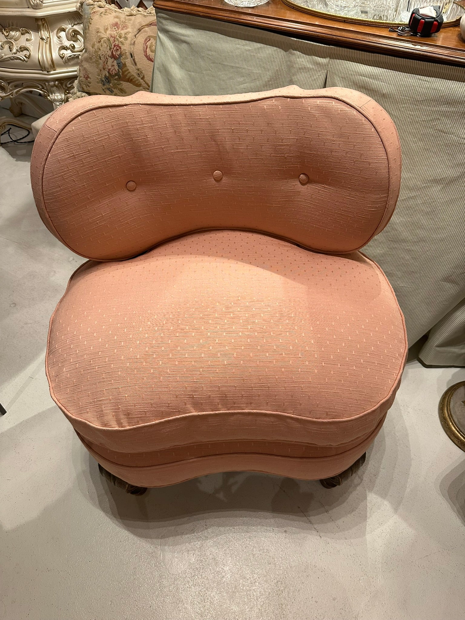 Antique pink coral boudoir chair, front view in showroom showing tufted back and curved seat