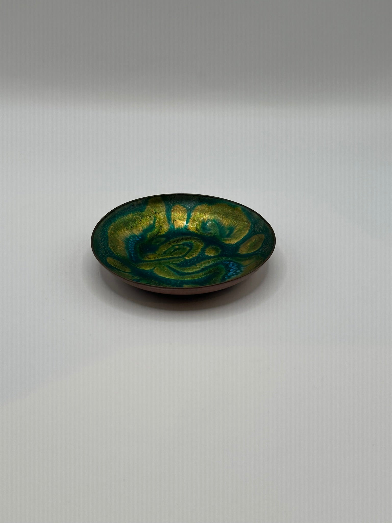 Doris Hall small green enamel dish, angled view of green-yellow swirl glaze with copper rim