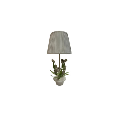 Vintage tole tulip and alabaster lamp with white pleated shade among other lamps on a white shelf