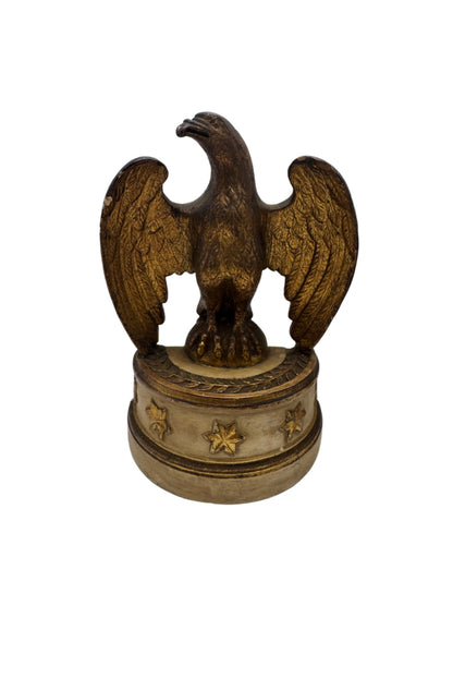 Single Borghese gilt eagle with raised wings on a cream pedestal base decorated with gold stars, front view