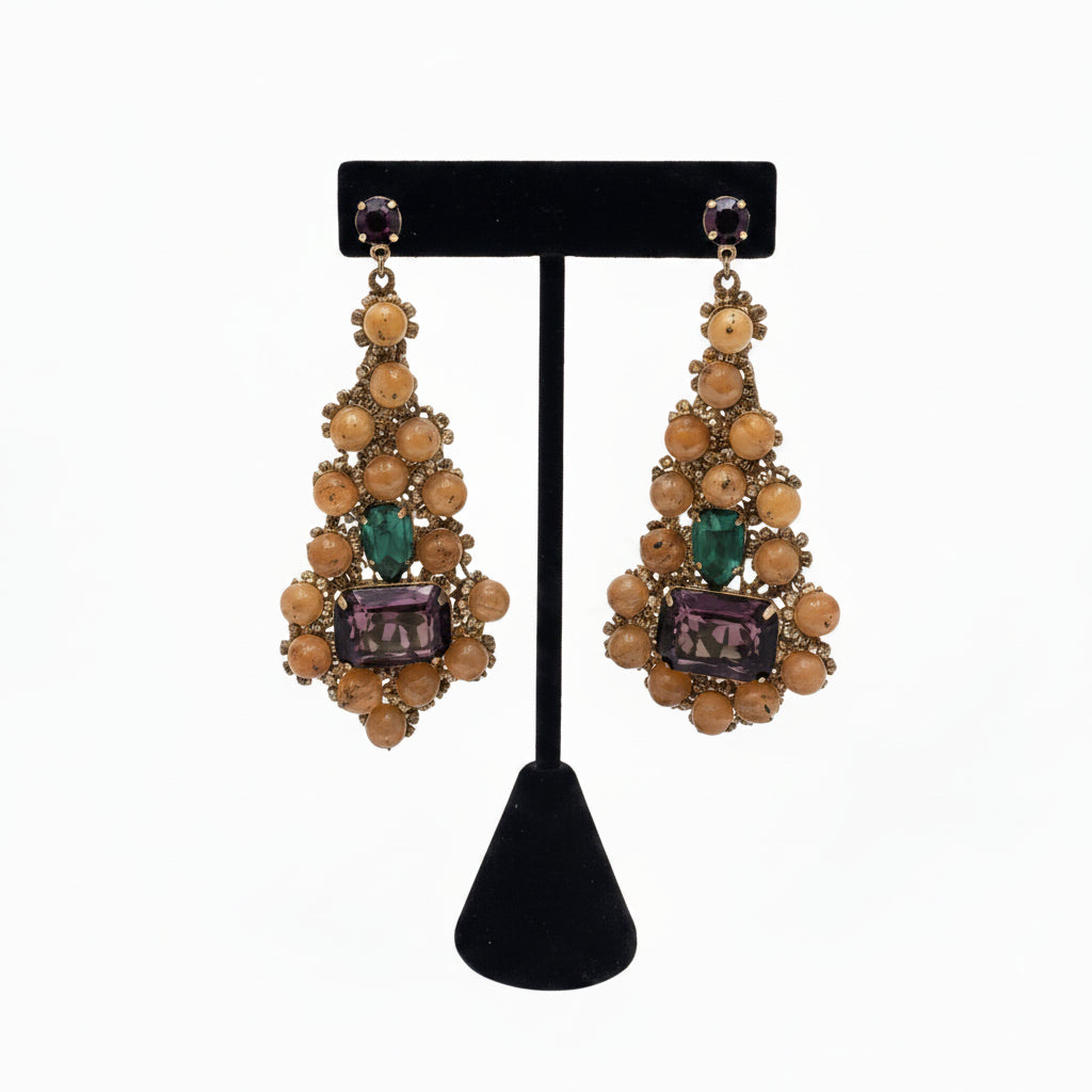Handwoven peach beaded teardrop earrings with green and purple gemstones, on a black display stand