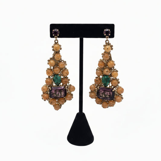 Handwoven peach beaded teardrop earrings with green and purple gemstones, on a black display stand