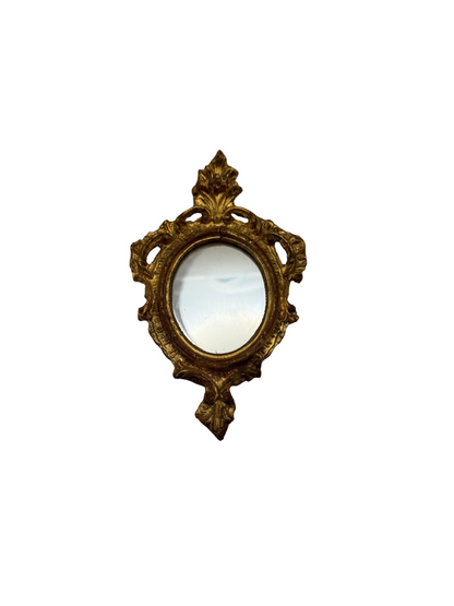 Petite Florentine oval mirror in ornate carved gilt frame with leafy crest, front view.