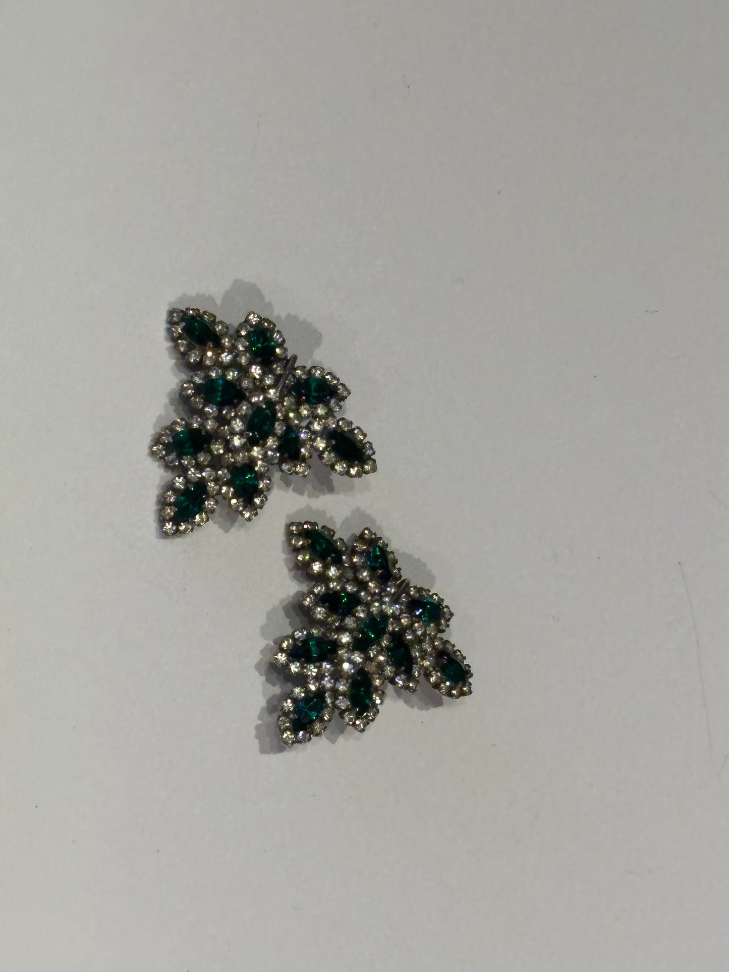 Vintage Les Bernard emerald and rhinestone leaf earrings, staggered pair, angled view.