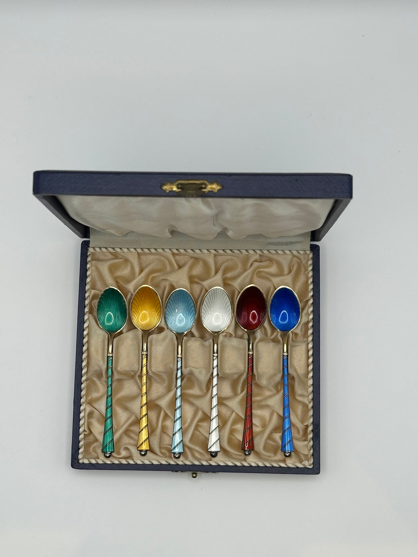 Danish enamel demitasse spoons in fitted navy box, six colored guilloché bowls with twisted sterling handles, upright.