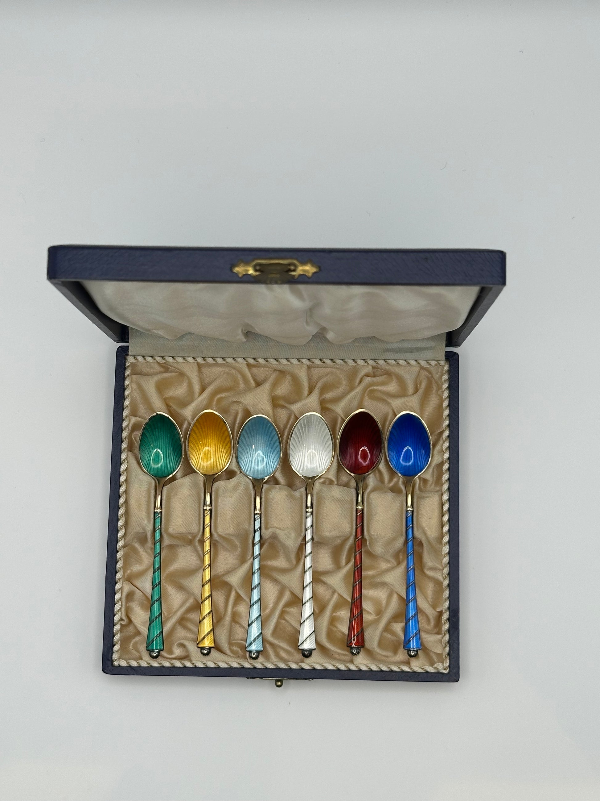 Danish enamel demitasse spoons in fitted navy box, six colored guilloché bowls with twisted sterling handles, upright.