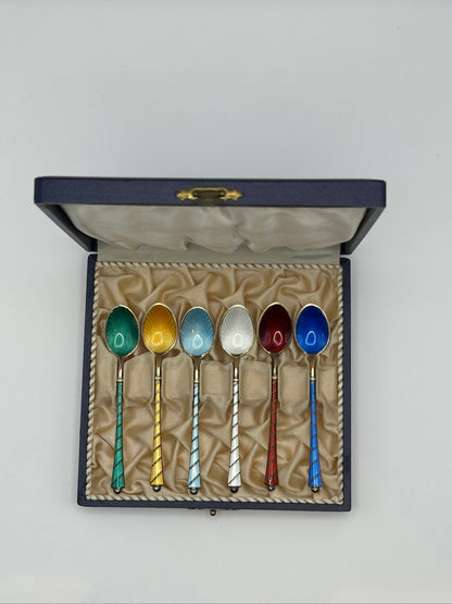 Six sterling and enamel demitasse spoons in navy presentation box, colored guilloché bowls and spiral handles, overhead view.