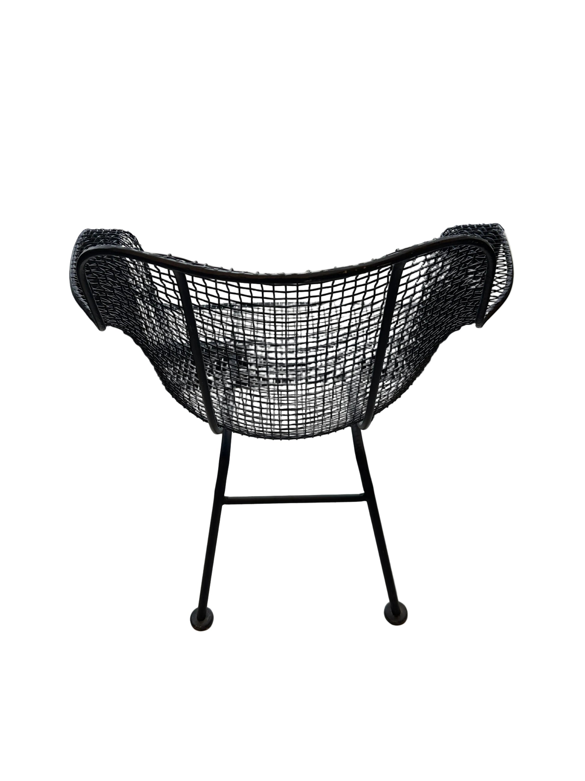 Rear view of black wire-mesh Russel Woodard chair on splayed iron legs