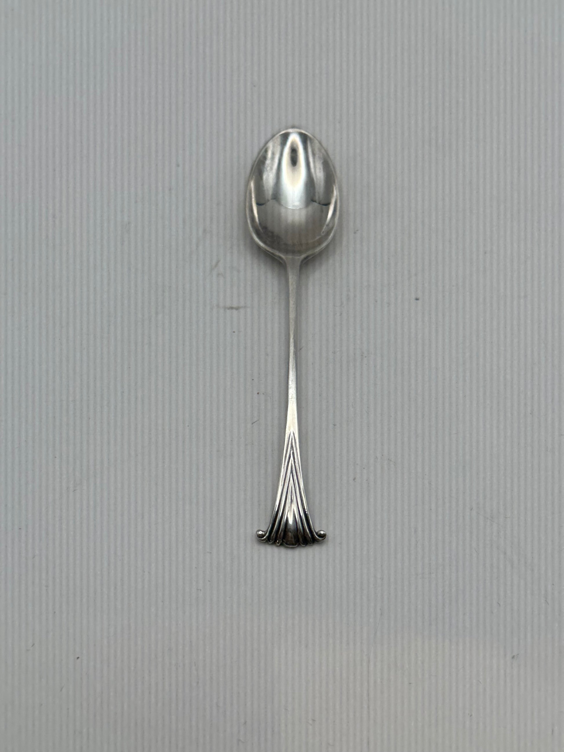 Single silverplate demitasse spoon, front view, oval bowl and slender handle with fanned scroll terminal
