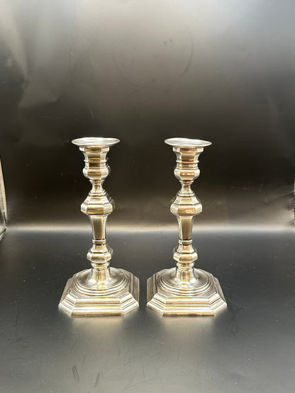 Pair of Georgian Revival silver plate candlesticks viewed against a dark reflective background
