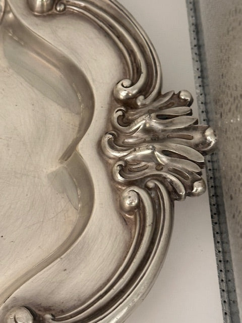 Close-up of silver plate tray's scrolled acanthus shell handle and ornate Rococo rim