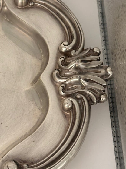 Close-up of silver plate tray's scrolled acanthus shell handle and ornate Rococo rim